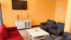 Una sala de estar con un sofá rojo, sofás grises, una mesa de centro blanca y un aparador blanco con adornos.