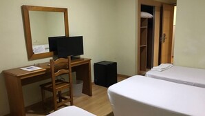 Una habitación de hotel con un escritorio de madera, un televisor, un cubo de basura pequeño y dos camas individuales.