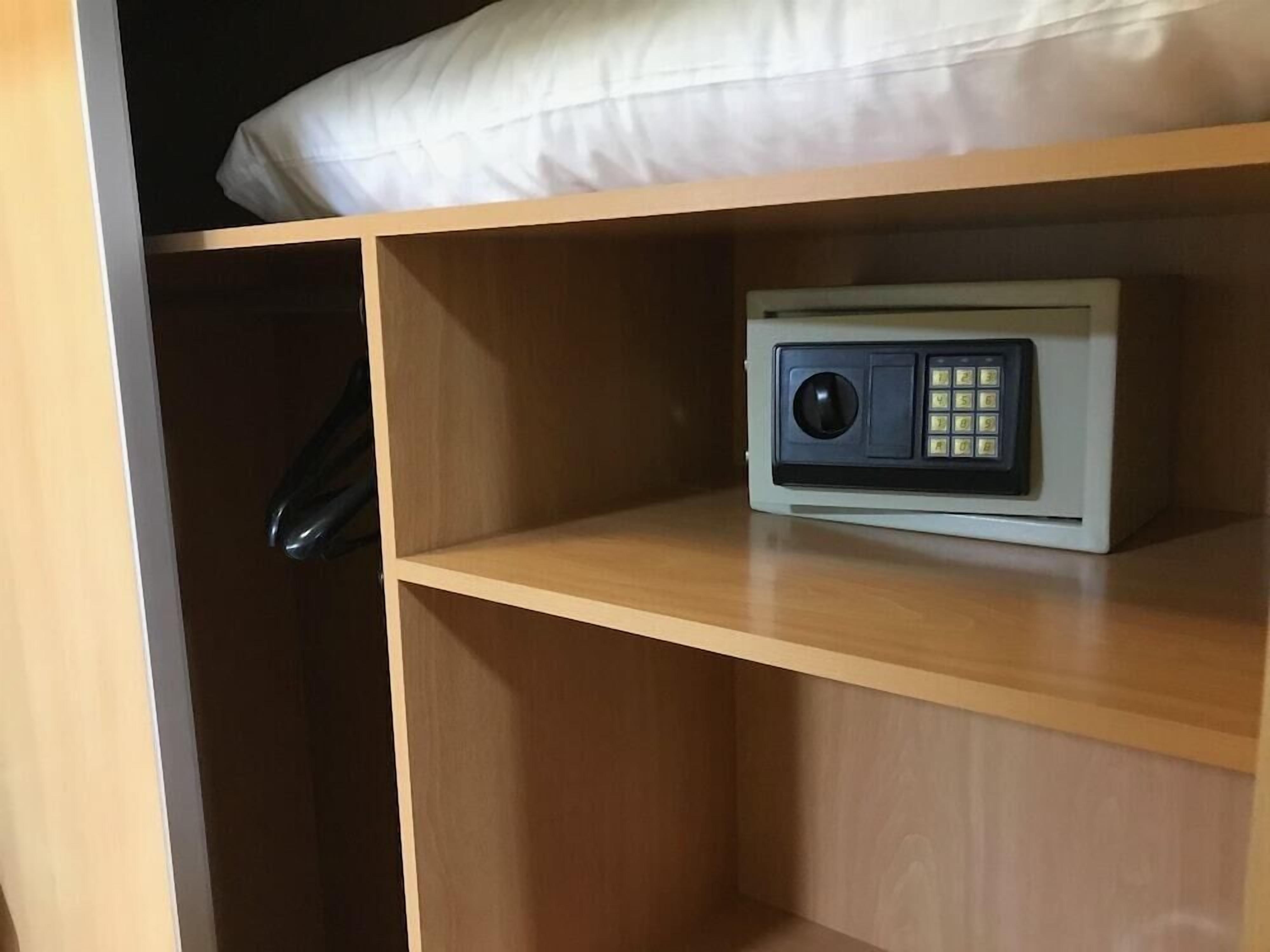 A room with a wooden shelf containing a small electronic device, a white pillow on the shelf, and a wooden wardrobe with a black handle.