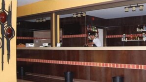 Zona de bar con mostrador, estanterías llenas de botellas y un elemento decorativo en la pared.
