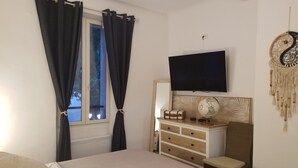 Una camera da letto con un letto, una cassettiera, una televisione e una finestra con tende.