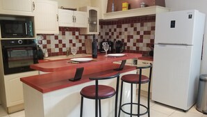 Una cucina moderna con mobili bianchi, un piano di lavoro rosso, forno a incasso, microonde, frigorifero e due sgabelli da bar.