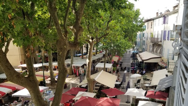 Un mercato all'aperto con tavoli e ombrelloni, immerso tra alberi ed edifici.