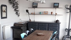 A dining area with a wooden table and chairs, a radiator, a black cabinet, and a ceiling light fixture. - Appartement vue mer (Veulettes Sur Mer)
