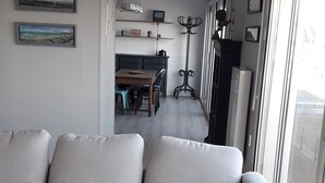 A modern living room with a grey sofa, a small round table, and a view of the dining area through a glass door. - Appartement vue mer (Veulettes Sur Mer)