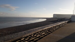 A coastal walkway with a stone wall and a paved path alongside a beach. - Appartement vue mer (Veulettes Sur Mer)