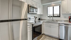 A modern kitchen with stainless steel appliances, white cabinetry, and a window providing natural light. - Family friendly condo, Ocean views (Tybee Island)