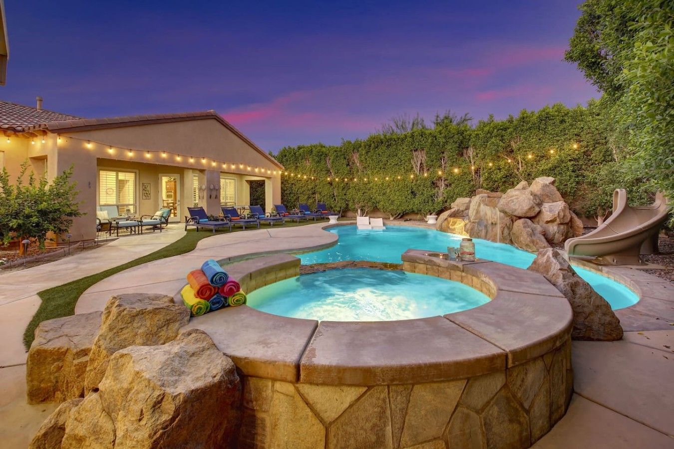 A swimming pool with a hot tub, lounge chairs, and a house in the background.