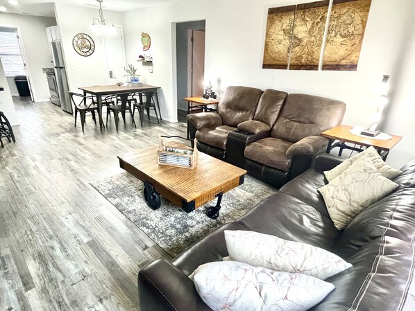 Ein Wohnzimmer mit Ledersofa, einem Holztisch und einem Essbereich mit Tisch und Stühlen.