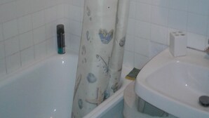 Une salle de bain avec une baignoire, un rideau de douche orné de motifs représentant des créatures marines, un lavabo blanc et une poubelle.