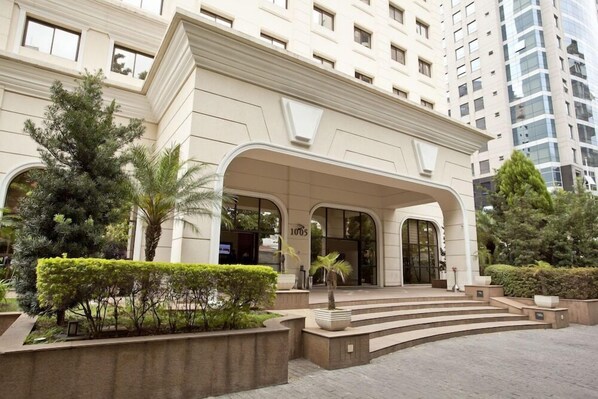 A modern hotel entrance with a grand archway, steps leading up to the doors, and well-maintained landscaping. - The World Hotels (São Paulo)