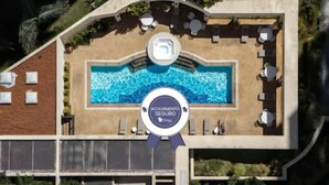 An aerial view of a hotel with a swimming pool surrounded by lounge chairs and tables, a poolside bar, and a certificate of safety. - The World Hotels (São Paulo)