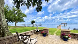 Un patio con una silla, una maceta de piedra con flores y vistas a un lago con muelle y mirador.