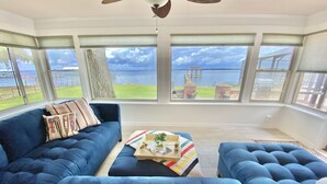 Un salón amplio con un sofá azul grande, una mesa de centro con adornos y vistas al mar a través de grandes ventanales.