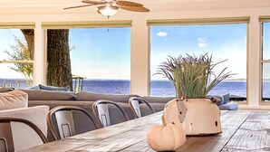 Una sala de estar moderna con un ventanal grande con vista al mar, un comedor con mesa de madera y un ventilador de techo.