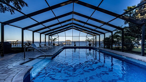 Una piscina al aire libre con zona cubierta, sillas de descanso y vistas al mar.