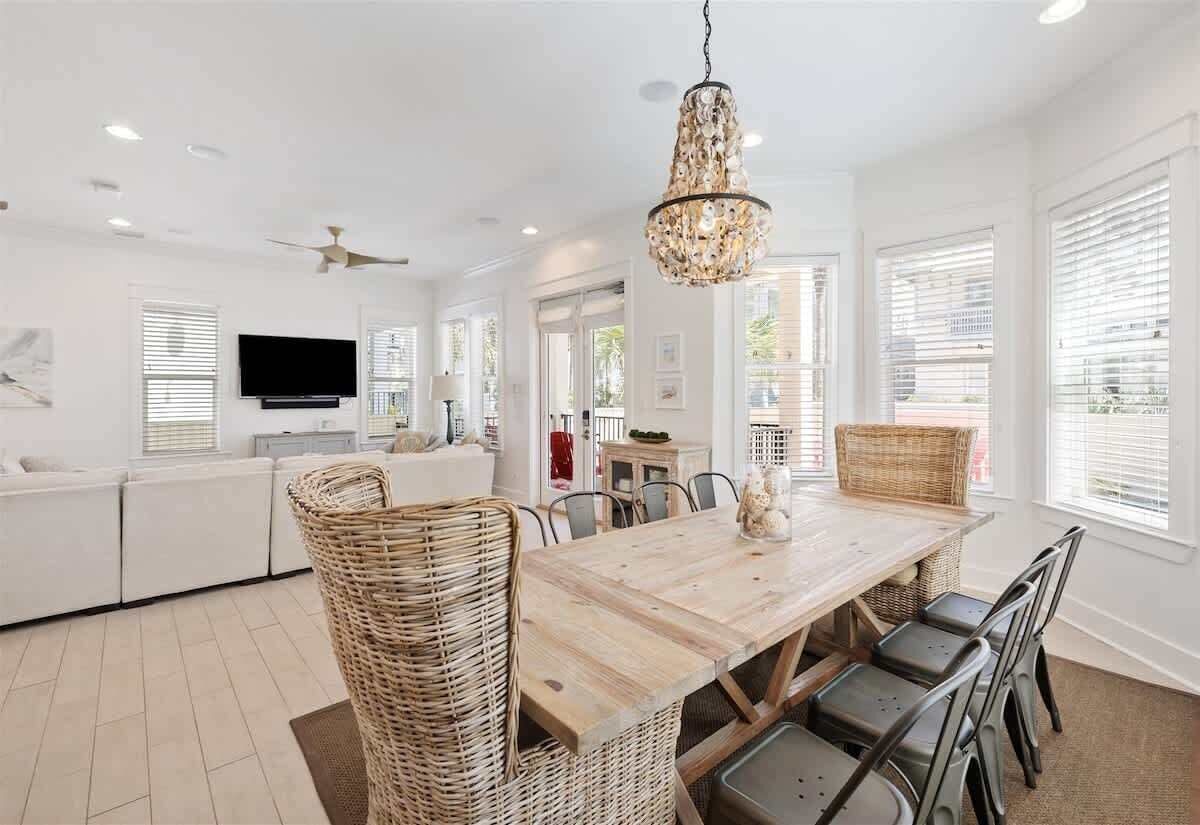 A modern kitchen with a dining table, wicker chairs, a chandelier, and a television.