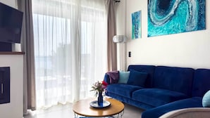 Een moderne woonkamer met een blauwe bank, een ronde salontafel met een bloevas, en een groot abstract schilderij aan de muur.