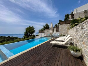 Una piscina a sfioro con un pontile in legno, sedie a sdraio e ombrelloni.
