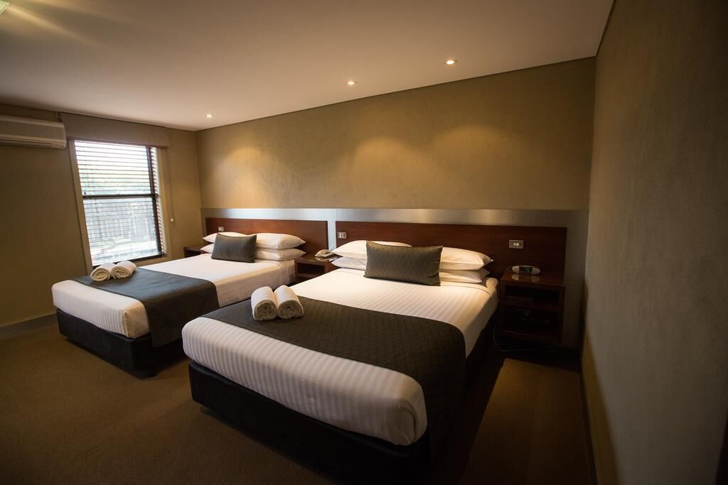 A hotel room with two beds, each with a pillow and a rolled towel.