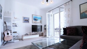 Una sala de estar moderna con una mesa de centro de vidrio, un sofá gris, un televisor y una guitarra.