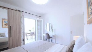 Habitación de hotel con cama, escritorio, silla, espejo y vista al exterior.