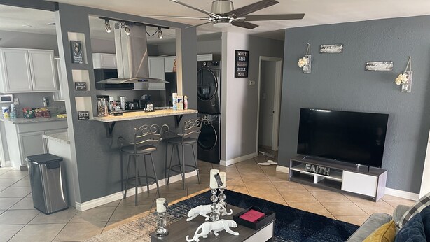 A modern living room with a TV, sofa, coffee table, and kitchen in the background. - SECURE FAMILY HOME/ VACATION/ WORK SPACE ECT. (NORTH LAS VEGAS, NV)