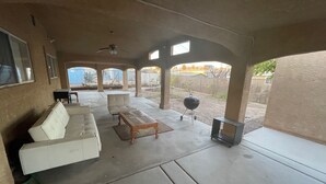 An outdoor patio area with a white sofa, a wooden table, and a barbecue grill. - SECURE FAMILY HOME/ VACATION/ WORK SPACE ECT. (NORTH LAS VEGAS, NV)