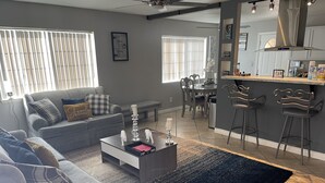 A modern living room with a grey sofa, a coffee table, and a dining area with a kitchen in the background. - SECURE FAMILY HOME/ VACATION/ WORK SPACE ECT. (NORTH LAS VEGAS, NV)