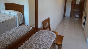A bedroom with a bed, a wooden chair, a table with a lace tablecloth, a mirror, and a door with a sign.
