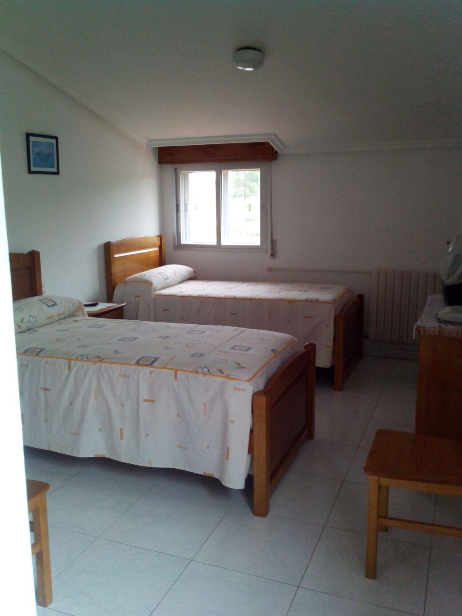 A bedroom with two single beds, a wooden headboard, a window, and a radiator.