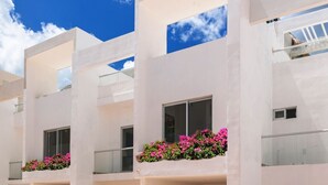 Un immeuble moderne à plusieurs étages, doté de balcons, de grandes fenêtres et d’une zone au rez-de-chaussée dallée.
