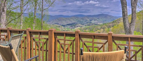A wooden deck with two wicker chairs facing a scenic view of mountains and a cloudy sky.