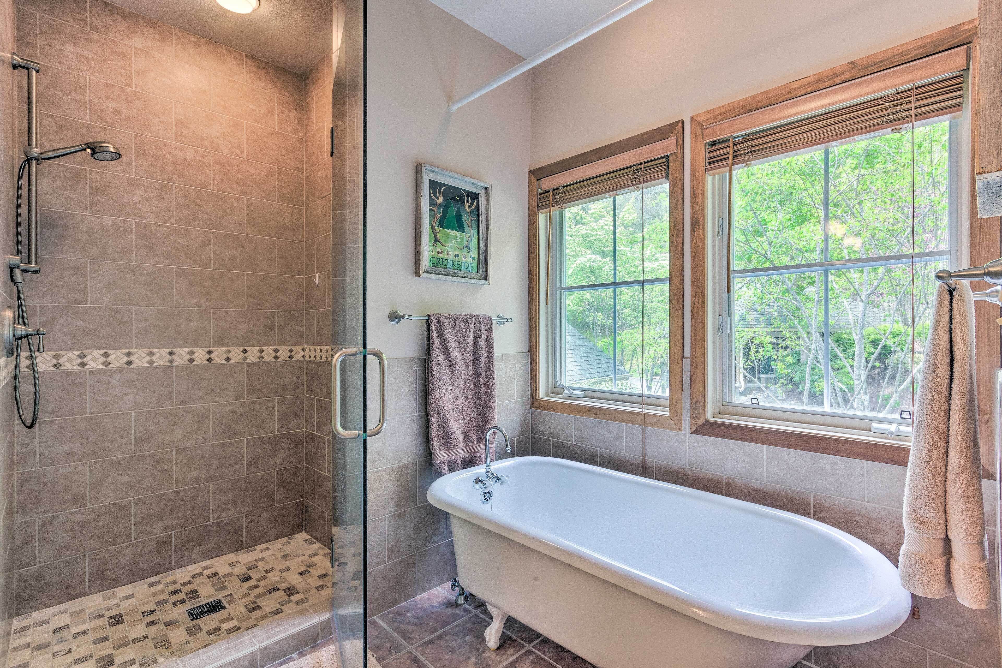 A bathroom with a walk-in shower, a freestanding bathtub, and a window with a view of trees.