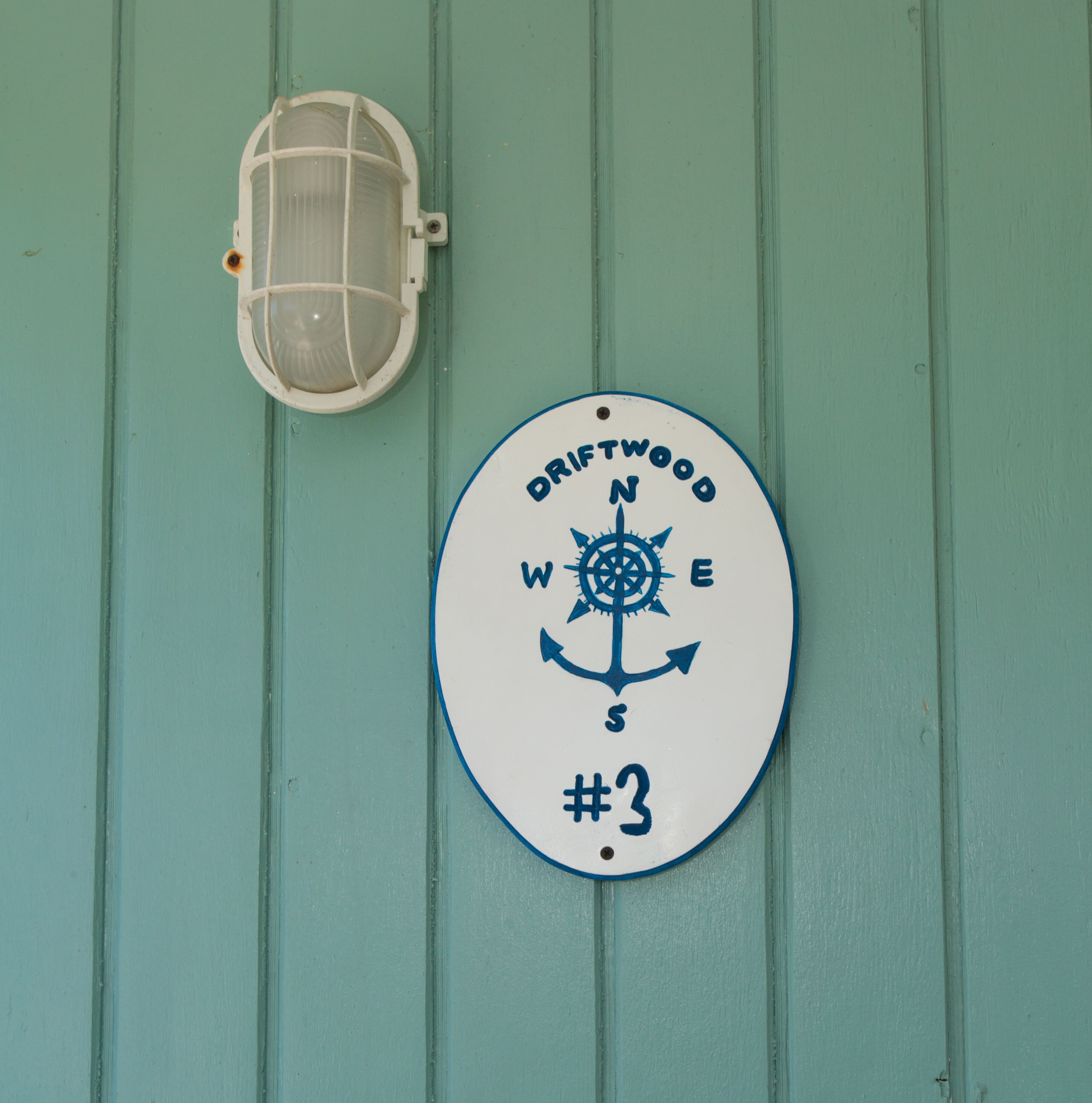 A wall-mounted sign with a compass and the text 'DRIFTWOOD #3' against a teal background.