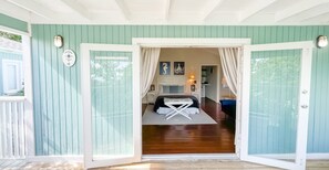 A room with a bed, a desk, and a chair. There is a door with curtains. - Ocean View Cottage, North Eleuthera, Driftwood Seahorse Cottage #3 (North Eleuthera)
