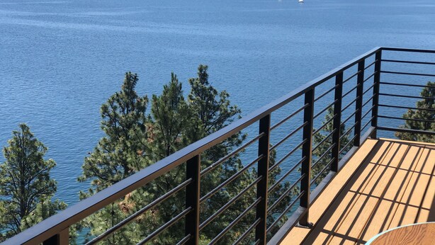 A wooden deck with a metal railing overlooking a calm body of water with sailboats.
