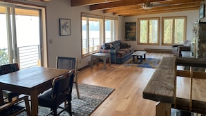 A spacious living room with a wooden ceiling, large windows, a stone fireplace, and a cozy seating area.