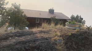A rustic cabin with a metal roof, surrounded by dry grass and a rocky terrain.