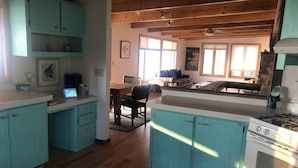A kitchen with teal cabinets, wooden flooring, and a central island. There is a dining area with a table and chairs, and a kitchen island with a stove.