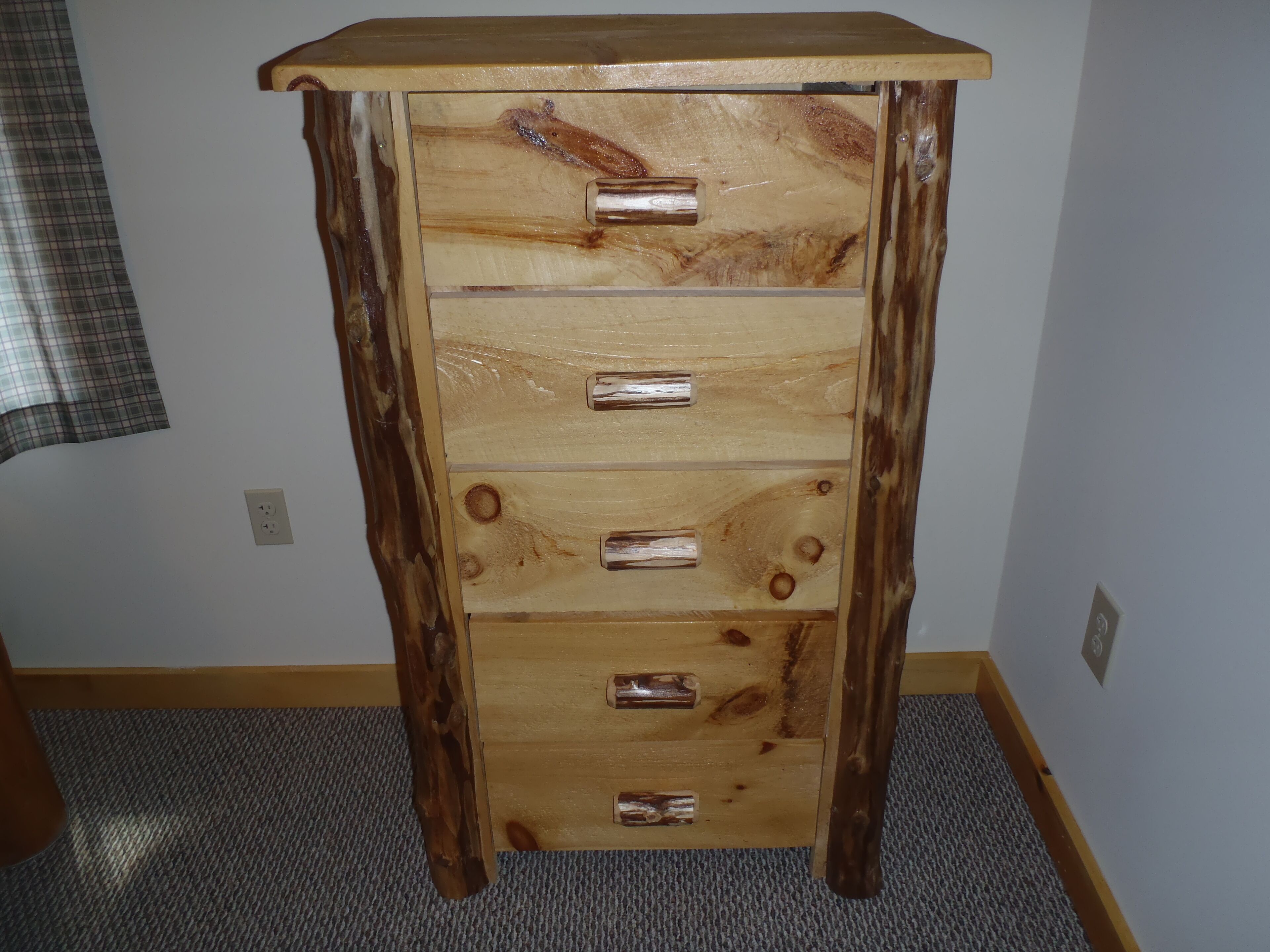 A wooden dresser with five drawers and a top shelf, featuring a natural wood finish and metal handles.