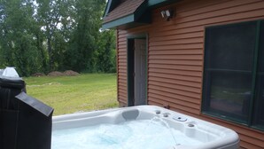 Un bain à remous à l’extérieur d’une maison, avec une pelouse et des arbres en arrière-plan.