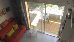 Una sala de estar con un sofá rojo, una mesita y un ventanal corredero que da a un espacio exterior con mesa y sillas.