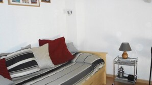Una cama individual con ropa de cama a rayas, un almohárraga roja y una mesita de noche pequeña con una lámpara.