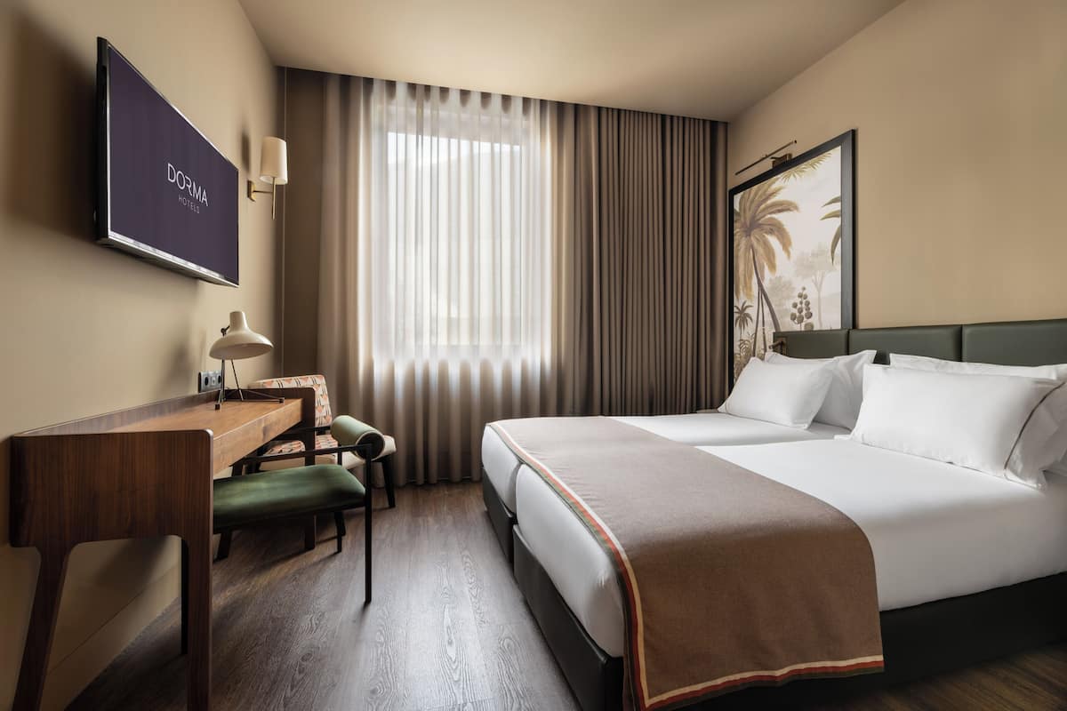 A hotel room with a bed, a desk, a chair, a television, and a large window with curtains.