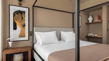 A modern hotel room with a four-poster bed, a bedside table with a lamp, a vase, and a framed artwork on the wall.