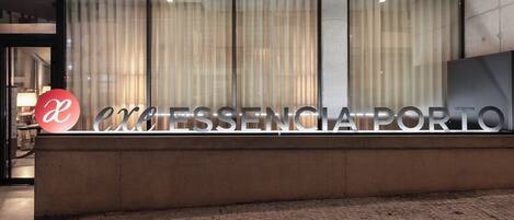 Una recepción con el rótulo "EXCESSENCIA PORTO" y un logotipo con una 'a' roja y una 'e' blanca.