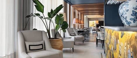 A modern hotel lobby with a seating area, large potted plants, and a decorative wall.