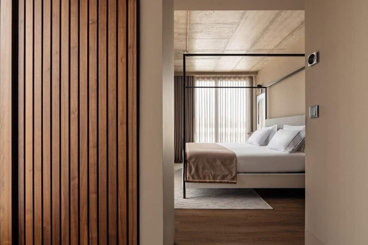 A modern bedroom with a bed, a wooden floor, and a window with blinds.