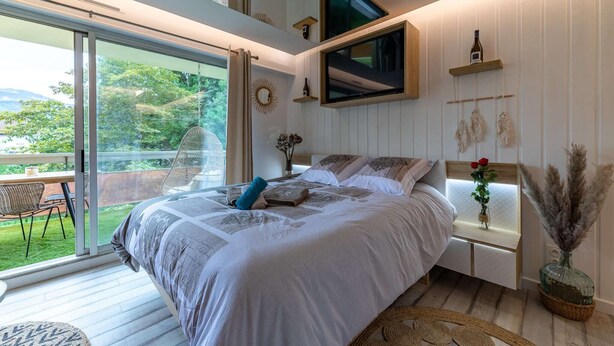 Een slaapkamer met een groot bed, een aan de muur bevestigde televisie, een klein tafeltje en uitzicht op het omliggende landschap.